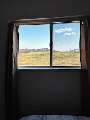 A room with a window overlooking a field and distant hills.