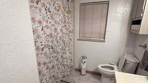 Ein Badezimmer mit Toilette, Bidet, Duschvorhang, Fenster mit Jalousien und Marmorboden.