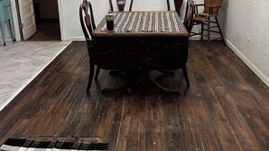 Ein Essbereich mit einem Holztisch, vier Stühlen, einer Kronleuchter und einem Kreuz an der Wand.