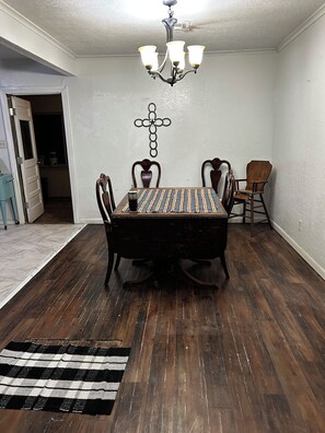 Un coin repas avec une table en bois, quatre chaises, un lustre et une croix accrochée au mur.