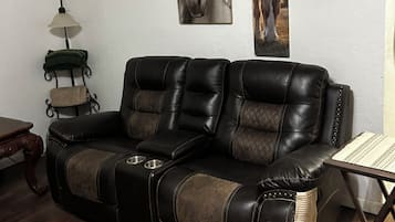 A leather sofa with a quilted pattern, a small table with a woven placemat, and wall-mounted artwork of horses.