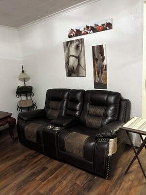 A leather sofa with a quilted pattern, a small table with a woven placemat, and wall-mounted artwork of horses. - Perfect 3-bedroom farmhouse with AC in tranquil Lone Wolf (Lone Wolf)
