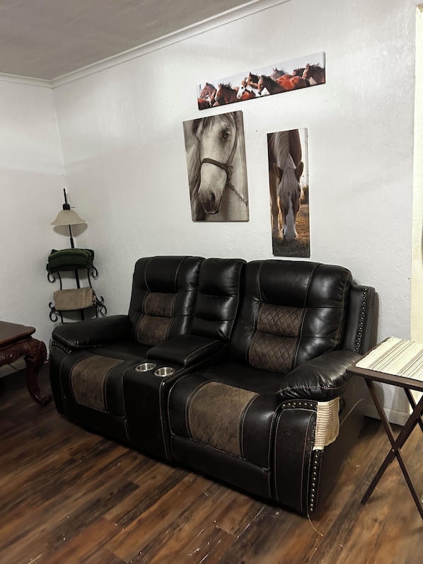A leather sofa with a quilted pattern, a small table with a woven placemat, and wall-mounted artwork of horses.