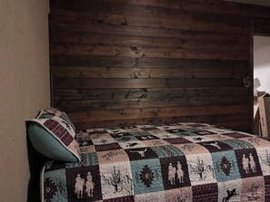 A room with a wooden headboard, a bed with a patterned quilt, and a wall-mounted lamp.
