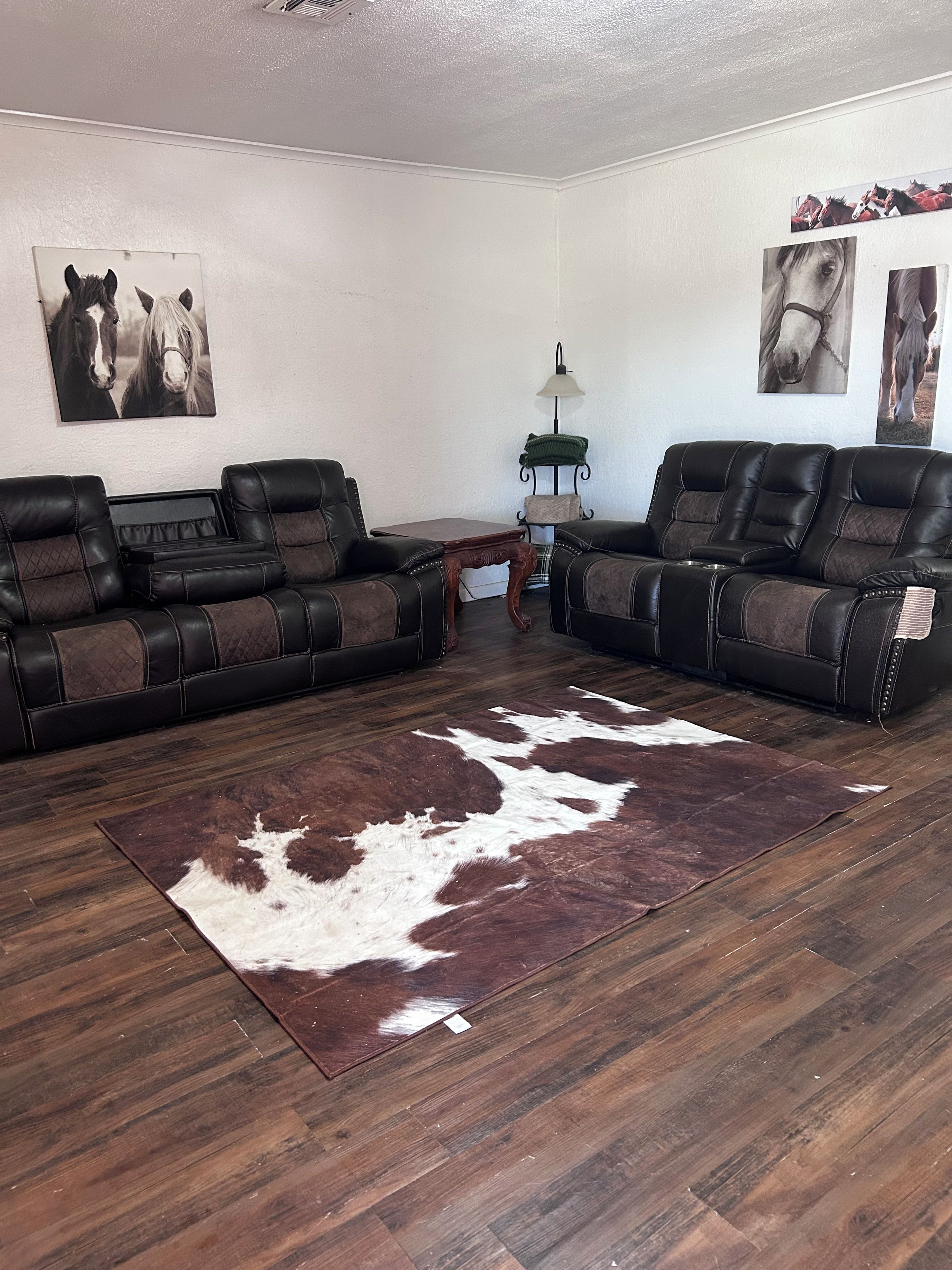 Un salon avec deux canapés en cuir, un tapis en peau de vache et des œuvres d’art murales sur le thème du cheval.