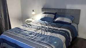 Ein Schlafzimmer mit einem Bett, einem Nachttisch, einer Lampe und einem dunklen Holzboden.