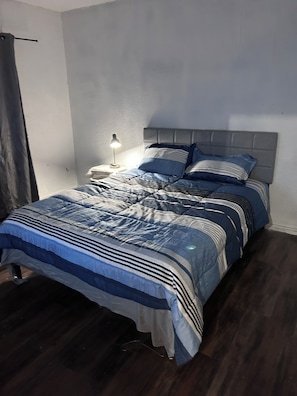 Une chambre à coucher avec un lit, une table de chevet, une lampe et un rideau.