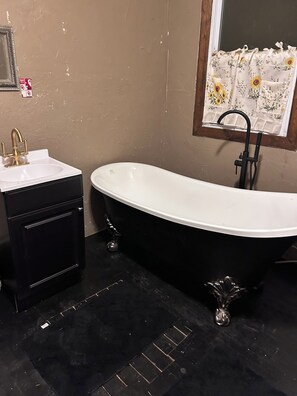 Un baño con una bañera negra, un lavamanos blanco y un espejo.