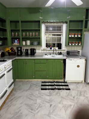 Una cocina con armarios verdes, una estufa blanca y un ventanal con persianas.