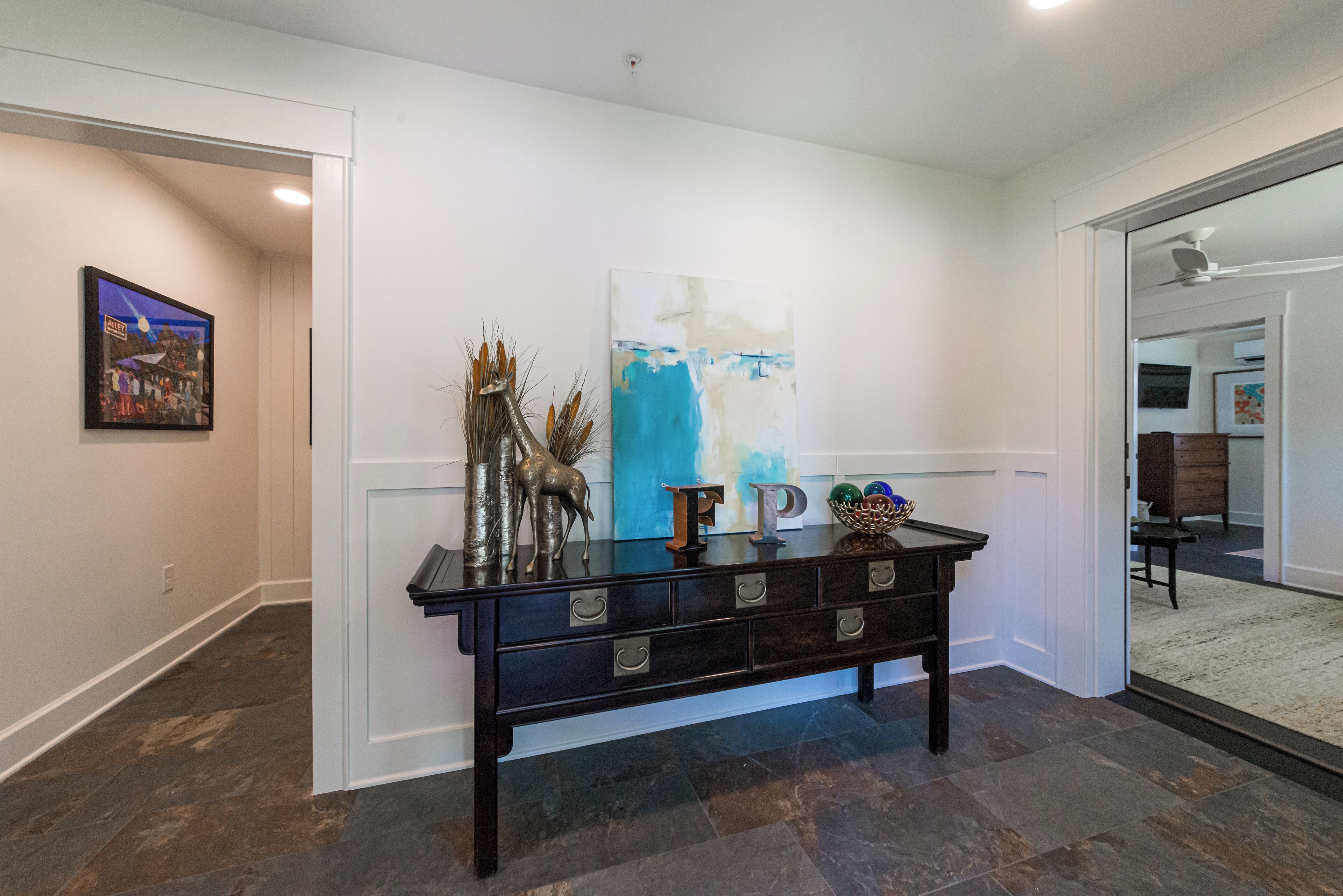 A hallway with a dark wooden console table, a painting, and a blue abstract painting on the wall.