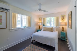 A bedroom with a bed, two bedside tables, a ceiling fan, and windows with curtains.