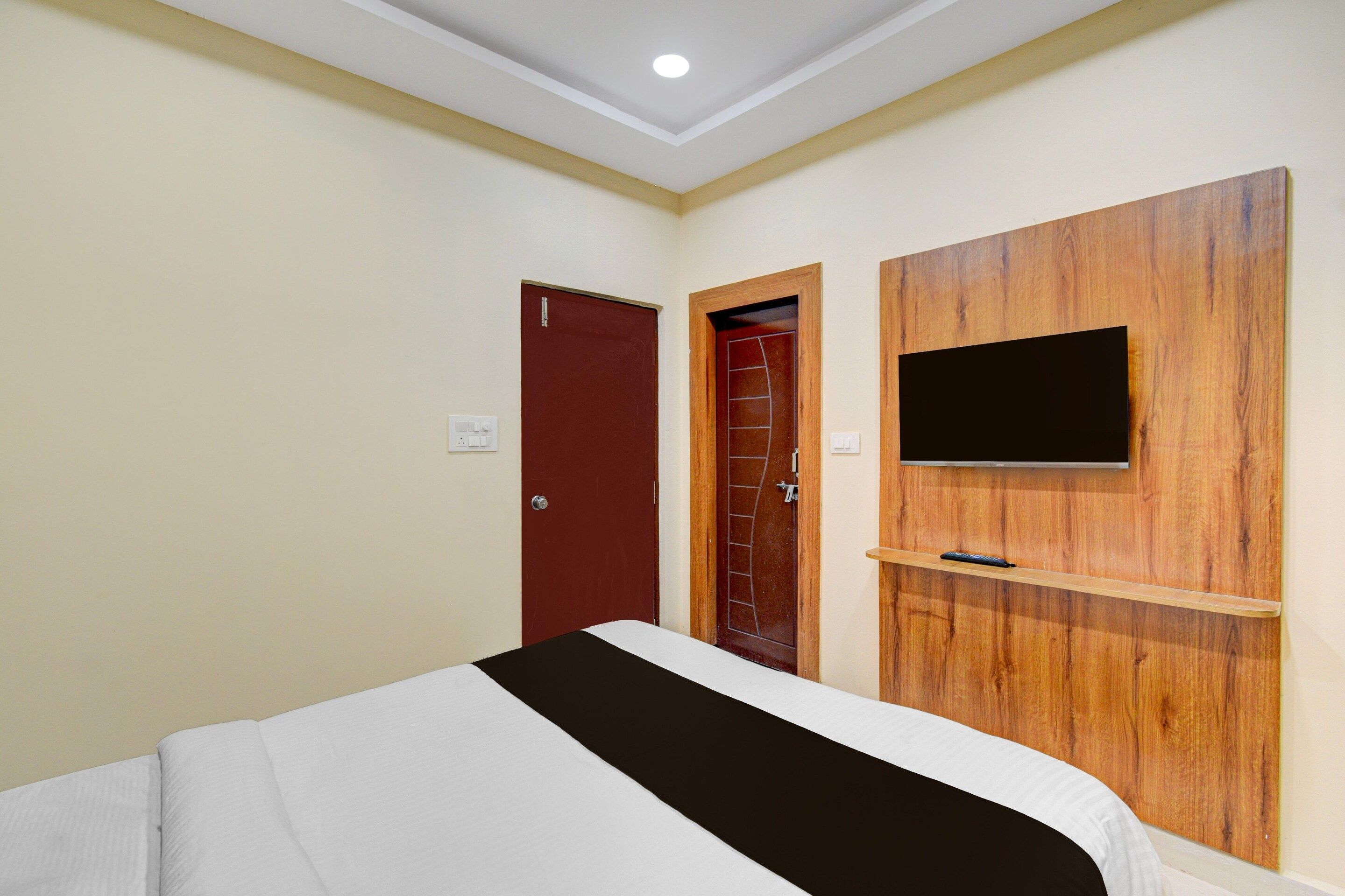 A hotel room with a bed, a wooden panel wall with a flat-screen TV, and two doors.