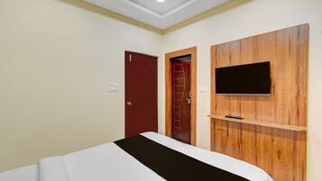 A hotel room with a bed, a wooden panel wall with a flat-screen TV, and two doors.