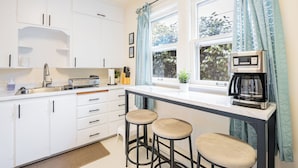 A kitchen with white cabinets, a countertop, a coffee machine, and two stools. - Cozy Olympia Cottage-Style Retreat in Capital area (Olympia)
