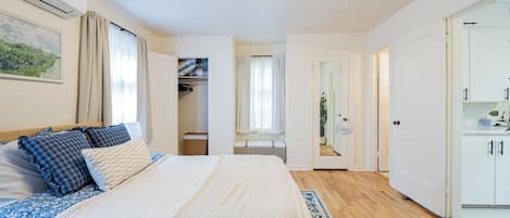 Une chambre à coucher avec un lit, des tables de chevet, une armoire et une salle de bain visible à travers une porte ouverte.