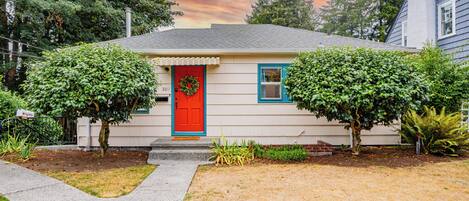 A single-story house with a red door, two small trees, and a well-maintained lawn.