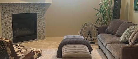 A living room with a fireplace, a sofa, an ottoman, and a television.