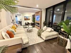 Ein modernes Wohnzimmer mit einem Ecksofa, einem Couchtisch und einem an der Wand montierten Fernseher.