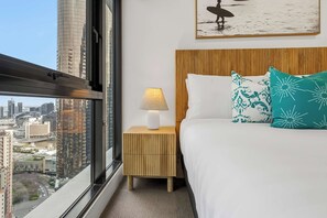 A hotel room with a bed, a nightstand with a lamp, a city view, and a framed picture on the wall. - 36th Floor Luxury 3BR  City Views Pool & 2 Cars (Southbank)