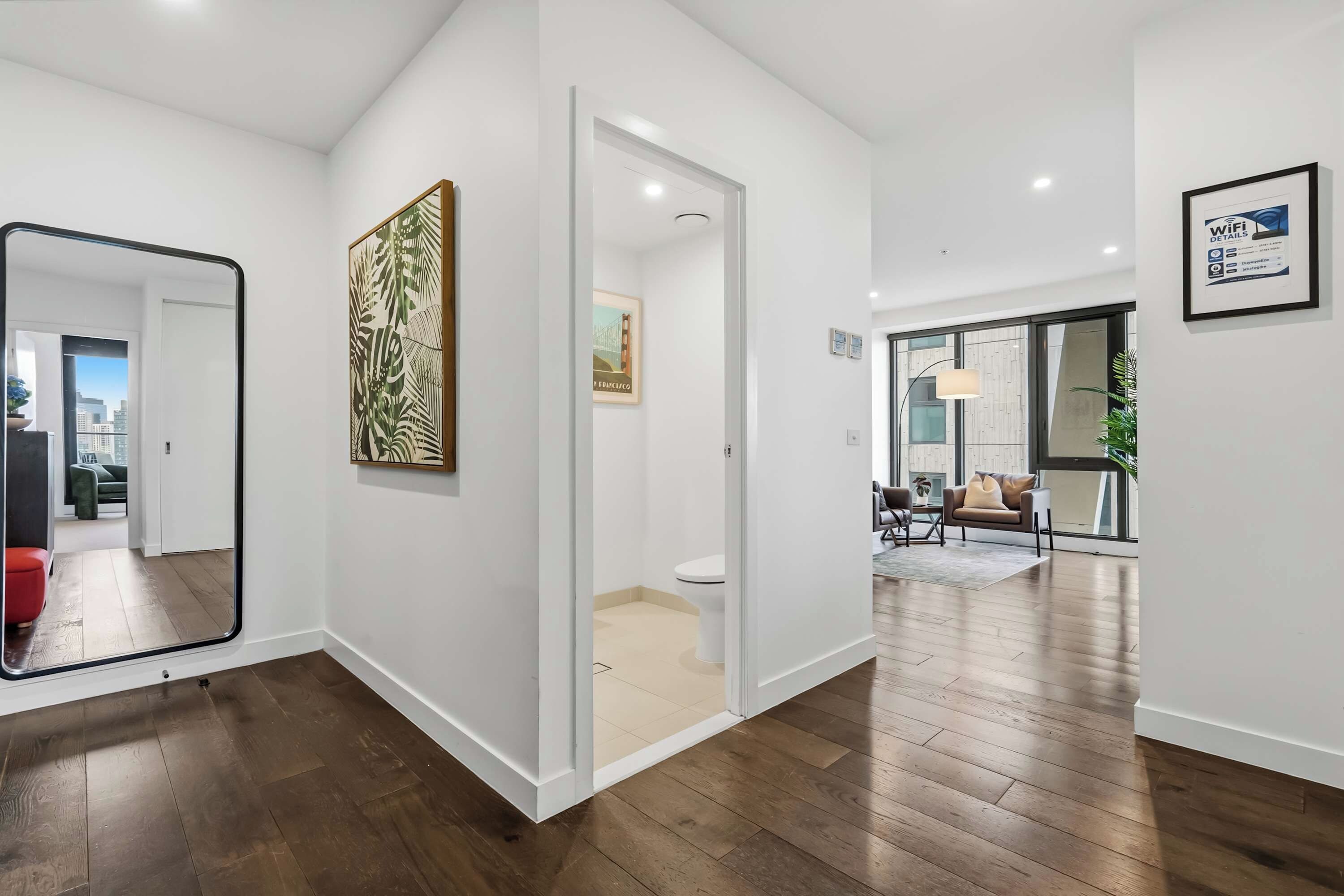 Un interior moderno con pisos de madera, un espejo grande, una impresi ón enmarcada de motivos tropicales y una puerta que conduce a otra habitación.
