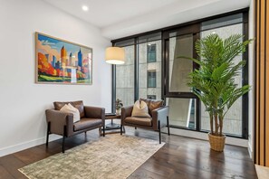 A modern living room with two leather sofas, a coffee table, a large potted plant, and a cityscape painting on the wall. - 36th Floor Luxury 3BR  City Views Pool & 2 Cars (Southbank)
