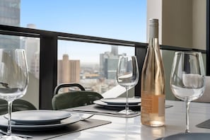 A dining table with wine glasses, a bottle, and a chair in a room with a city view. - 36th Floor Luxury 3BR  City Views Pool & 2 Cars (Southbank)