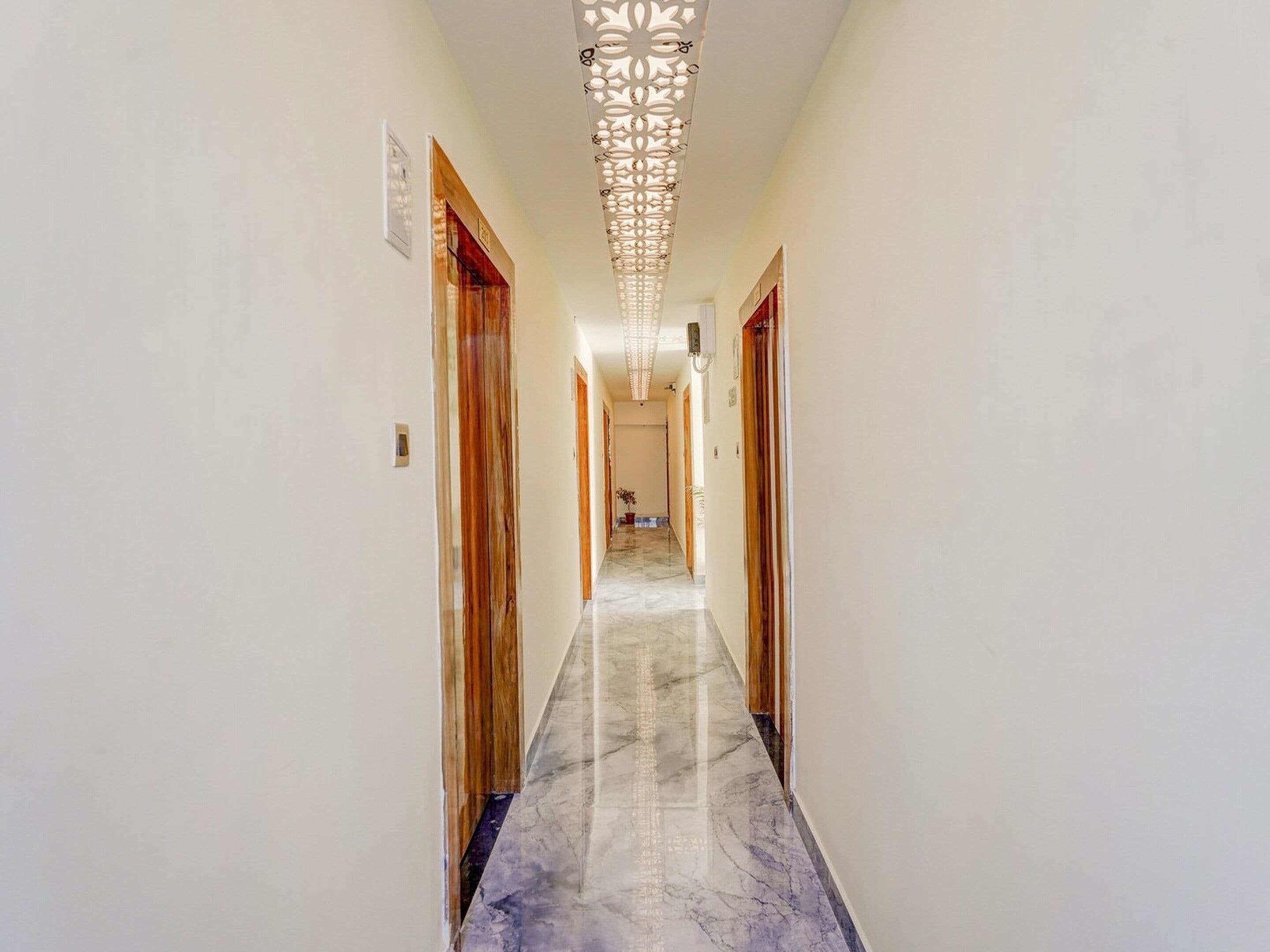 A hallway with marble flooring, wooden doors, and a decorative ceiling light fixture.