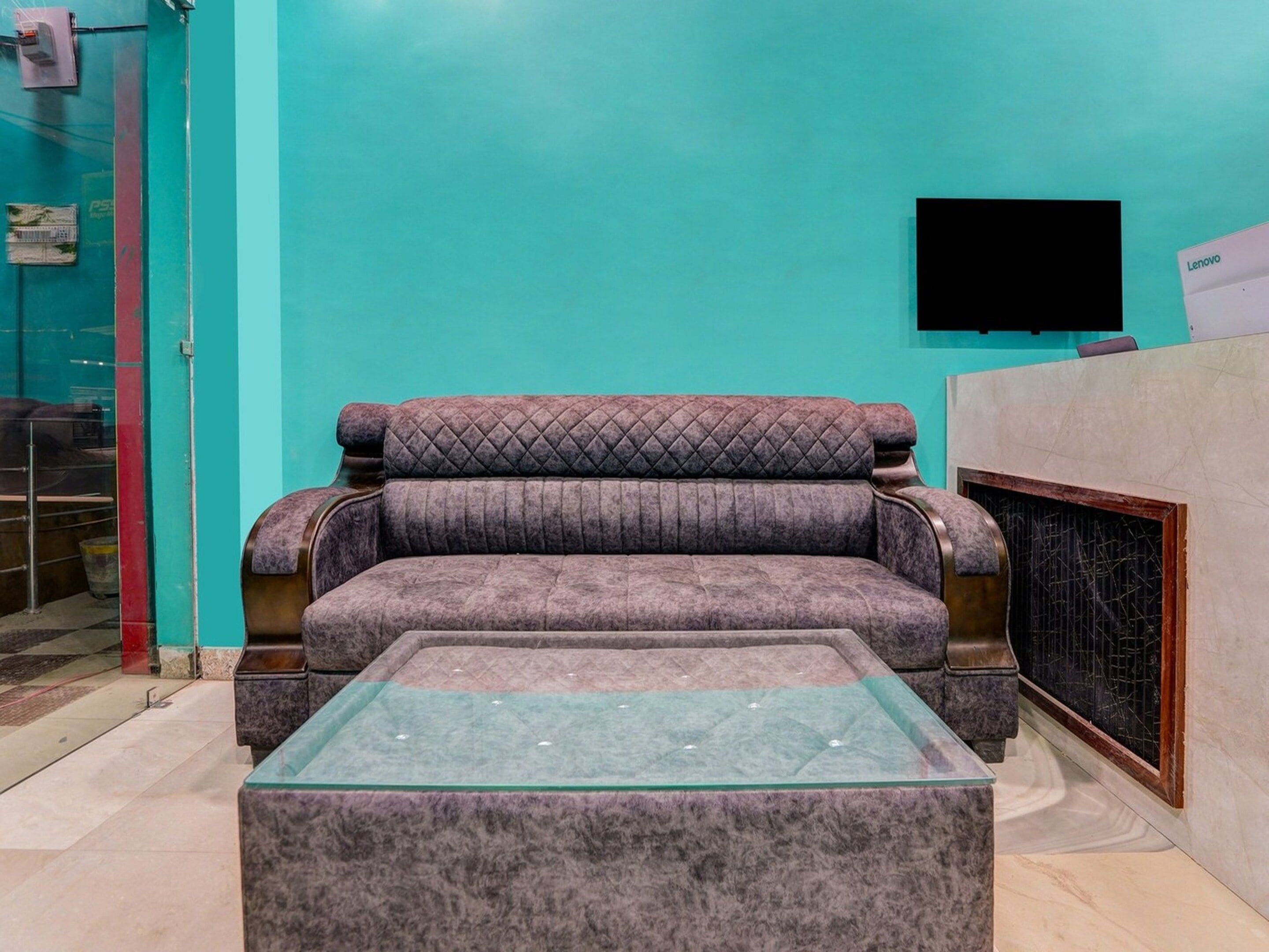 A room with a sofa, a glass-top coffee table, a television mounted on the wall, and a tiled floor.