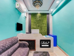 A reception area with a reception desk, a sofa, a wall-mounted TV, and a green wall with a textured pattern. - Deluxe Hotel Sapphire Grand (Ranchi)