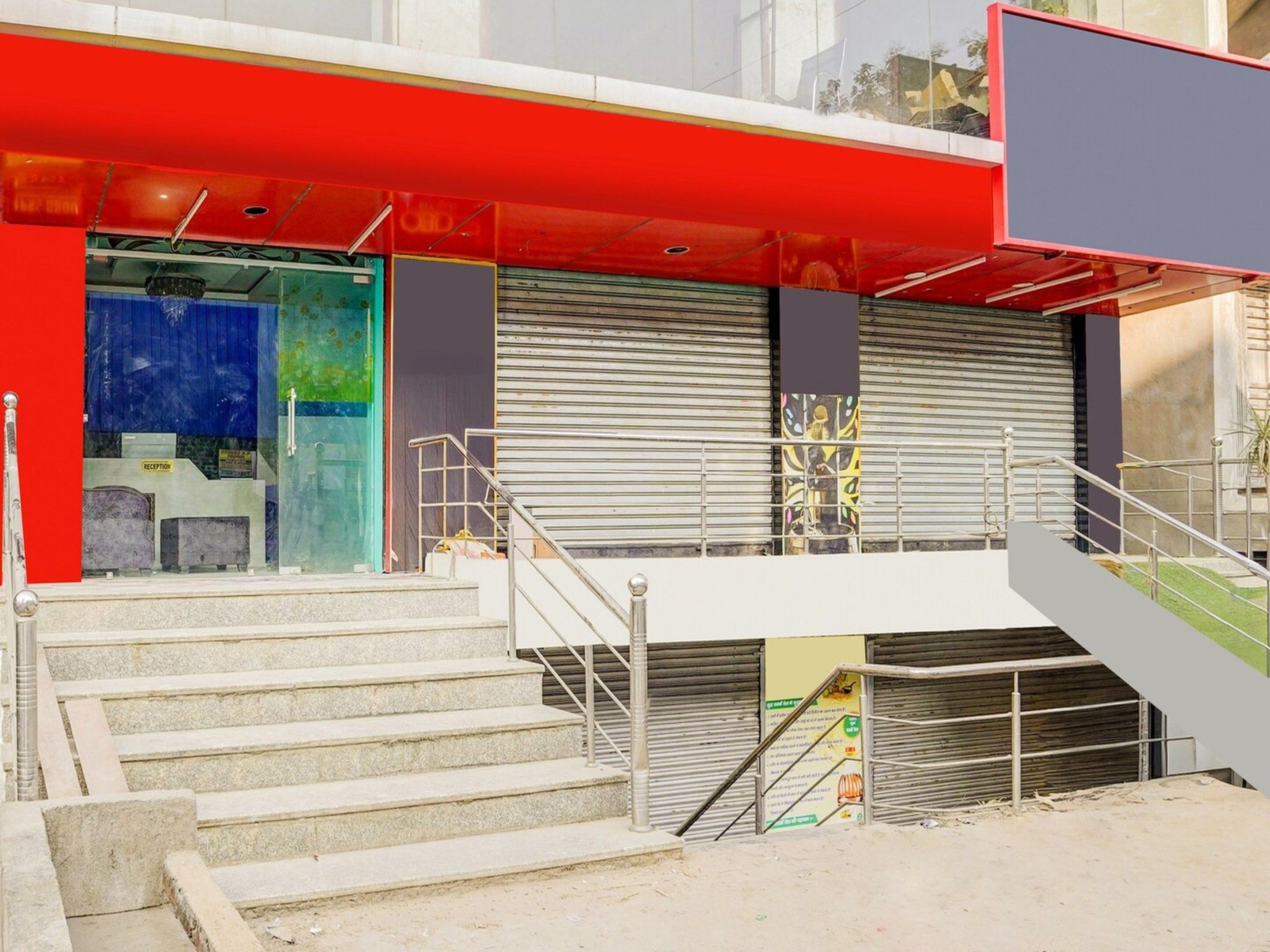 Un edificio con fachada roja, una zona de recepción y una escalera que sube a un nivel superior.