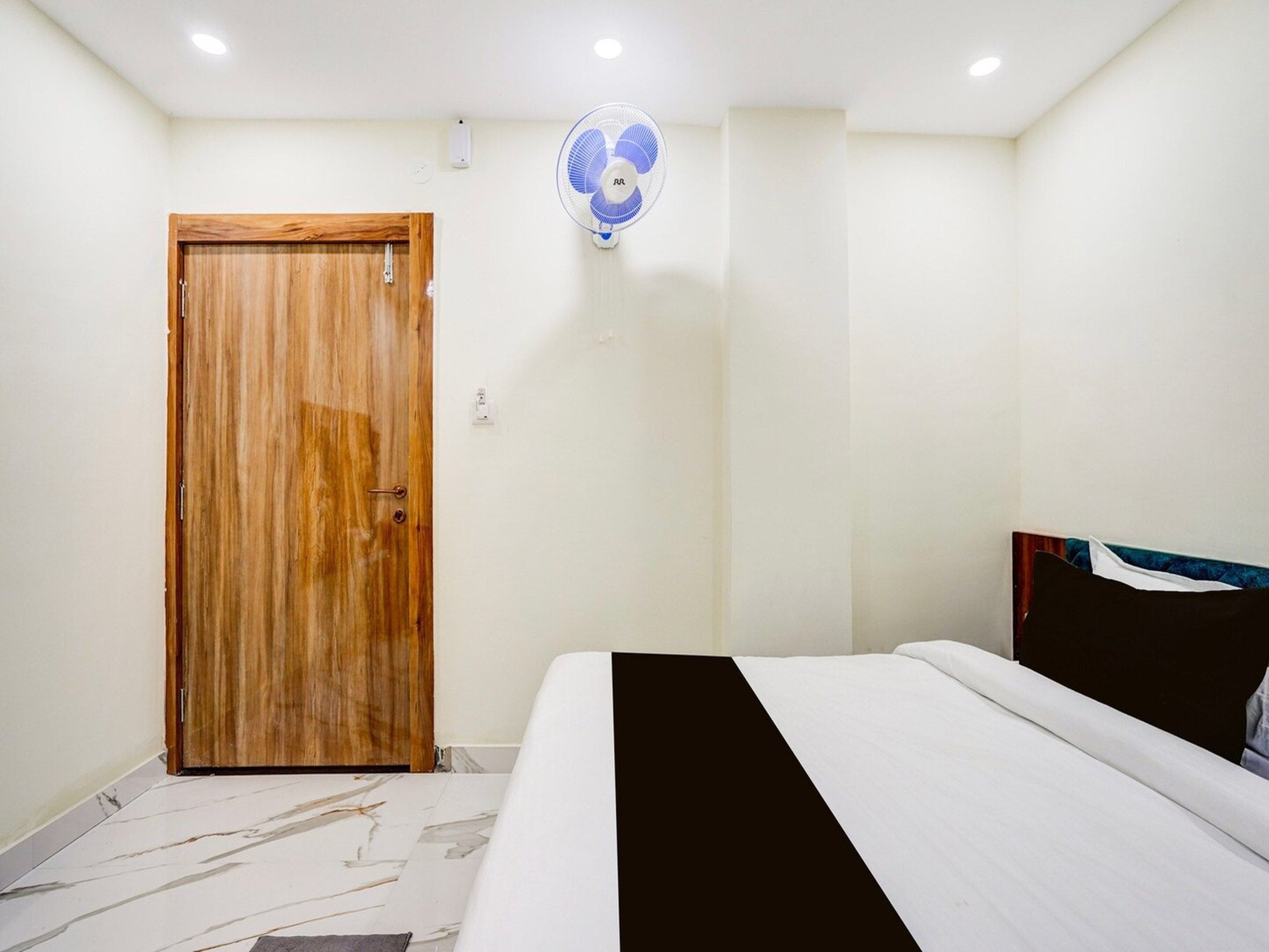 Un dormitorio con puerta de madera, una cama con colcha blanco y negro, y un ventilador de techo.