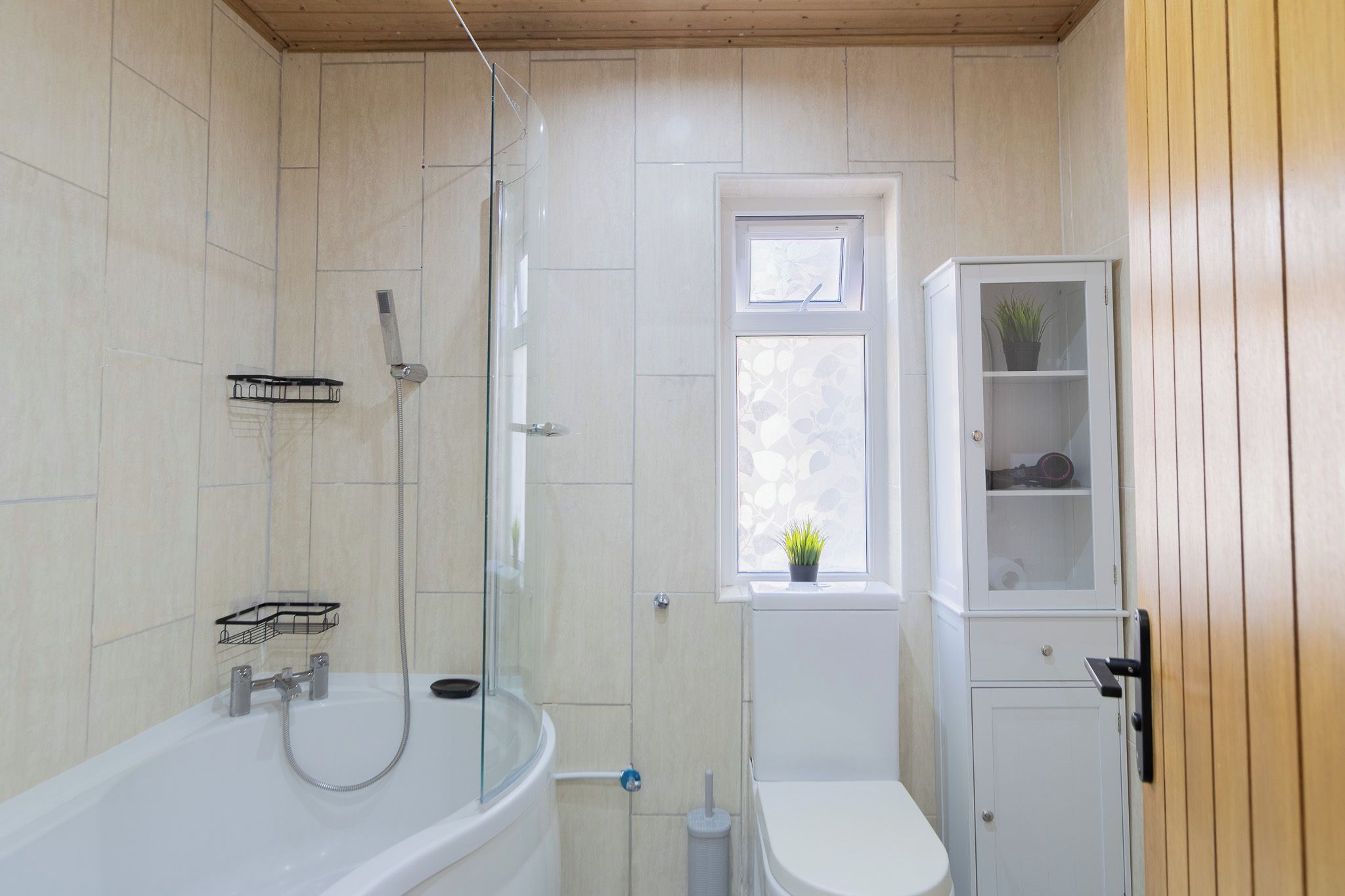 A bathroom with a bathtub, toilet, and a window with a plant.