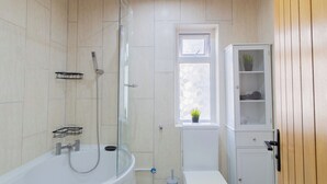 Een badkamer met een bad, toilet en raam met een plant.