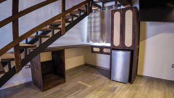 A compact kitchen with a built-in refrigerator, wooden staircase, and a small seating area.