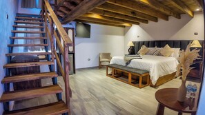 Un dormitorio con una escalera de madera, una cama con cabecera, una mesita de noche con una lámpara y una pequeña mesa con un florero y botellas de agua.