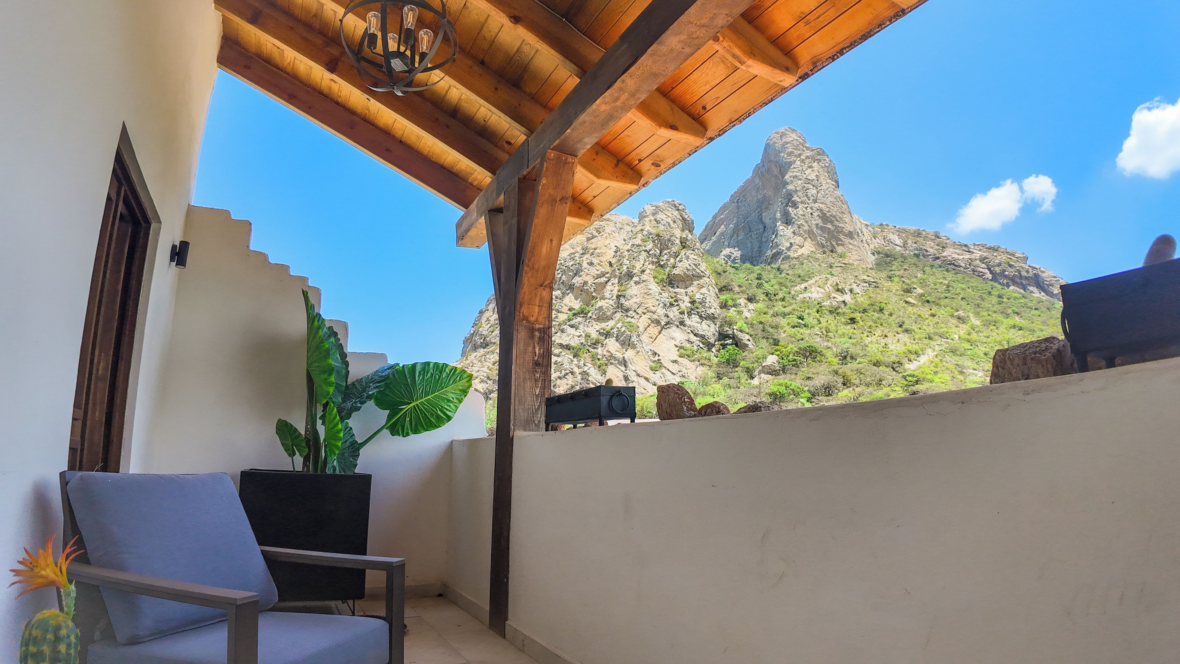 Un balcón con una silla, una planta en maceta y vistas a una montaña rocosa.