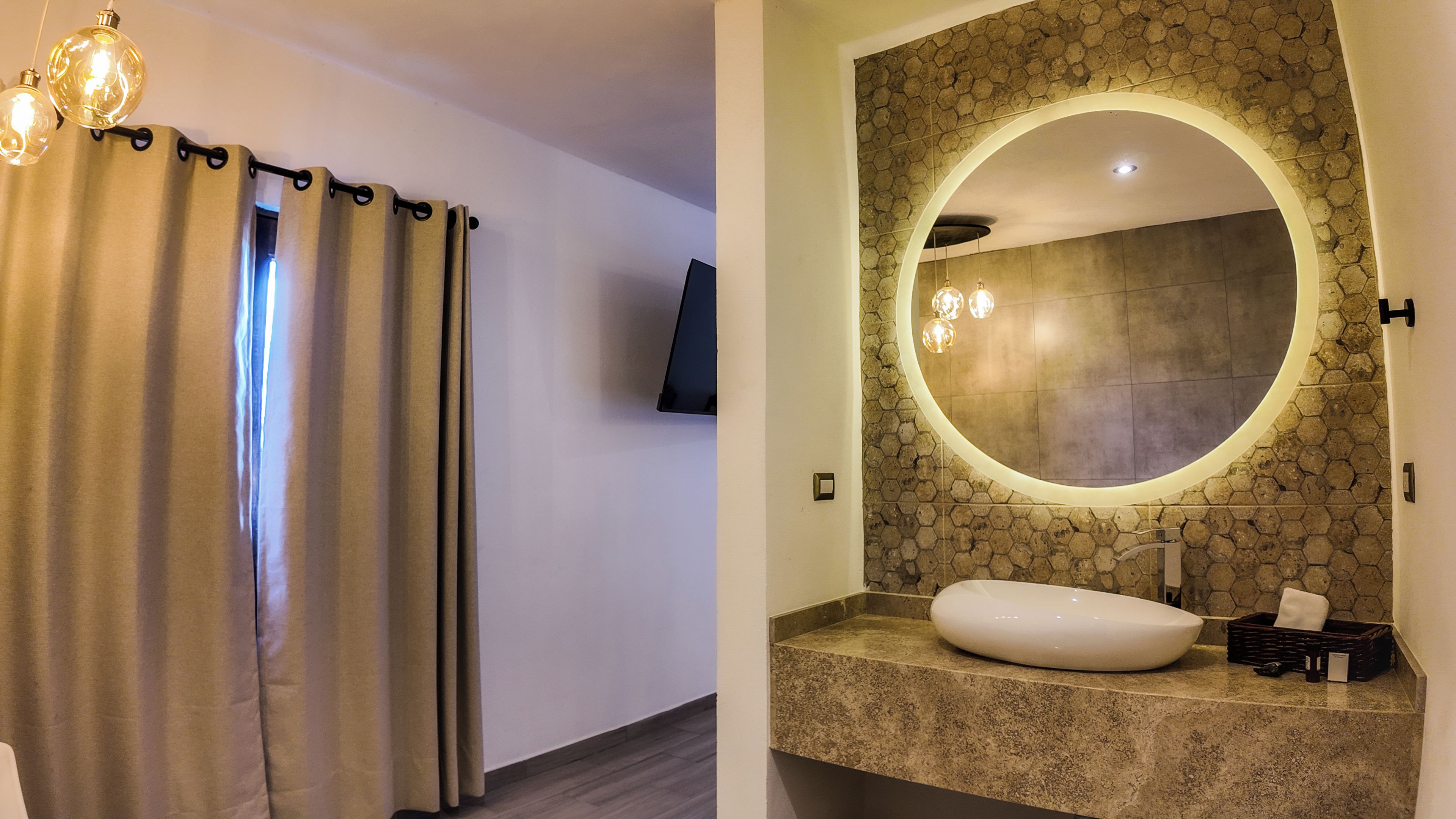 Un baño con espejo redondo, lavamanos y zona de ducha.