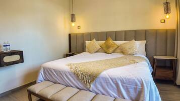 A neatly made bed with a headboard, a bedside table, a bench, and two wall-mounted lamps.