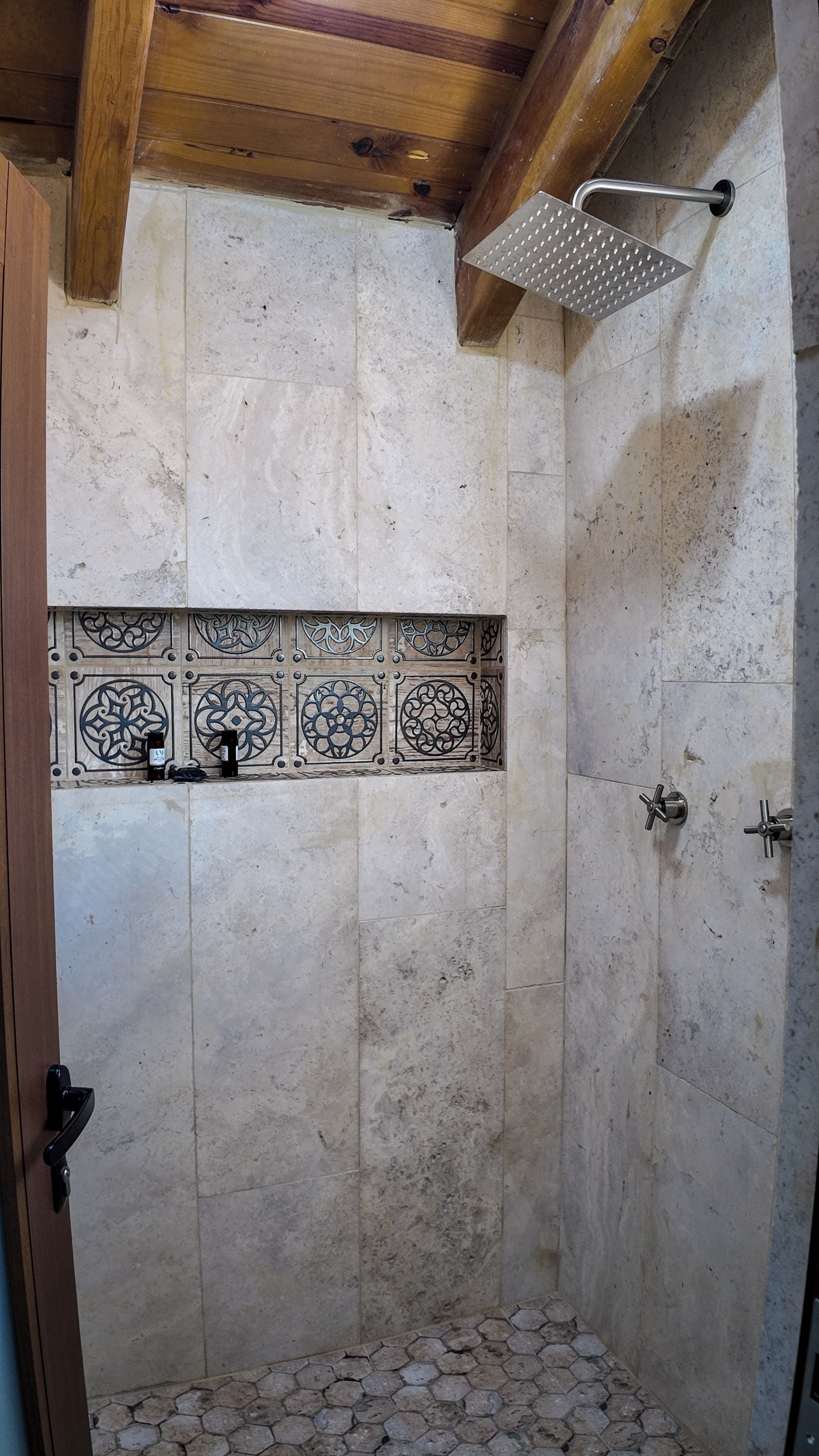 Una ducha con pared de azulejos, techo de madera y suelo de baldosas hexagonales.