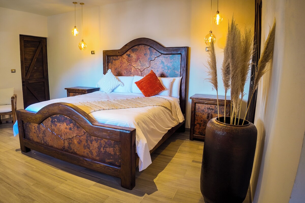 Ein Schlafzimmer mit einem hölzernen Bett, einem Nachttisch, einem Stuhl und einer großen Vase mit Pampasgras.