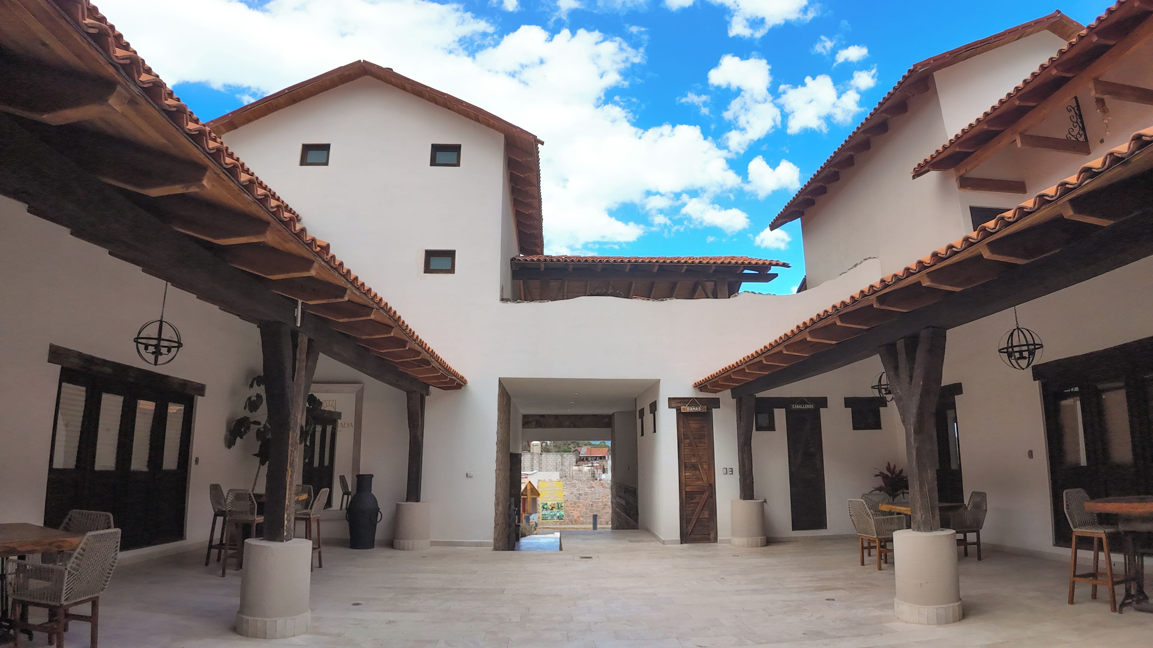Un patio con una puerta central que da a una calle, rodeado de paredes blancas y vigas de madera.
