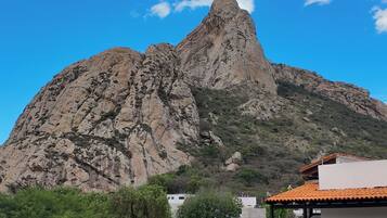 A mountain with a rocky peak, a white building with a red roof, and a garden with cacti and rocks.