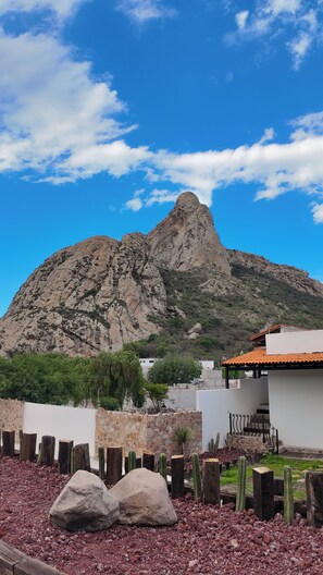 A mountain with a rocky peak, a white building with a red roof, and a garden with cacti and rocks. - Hotel Peña Dorada (Bernal)