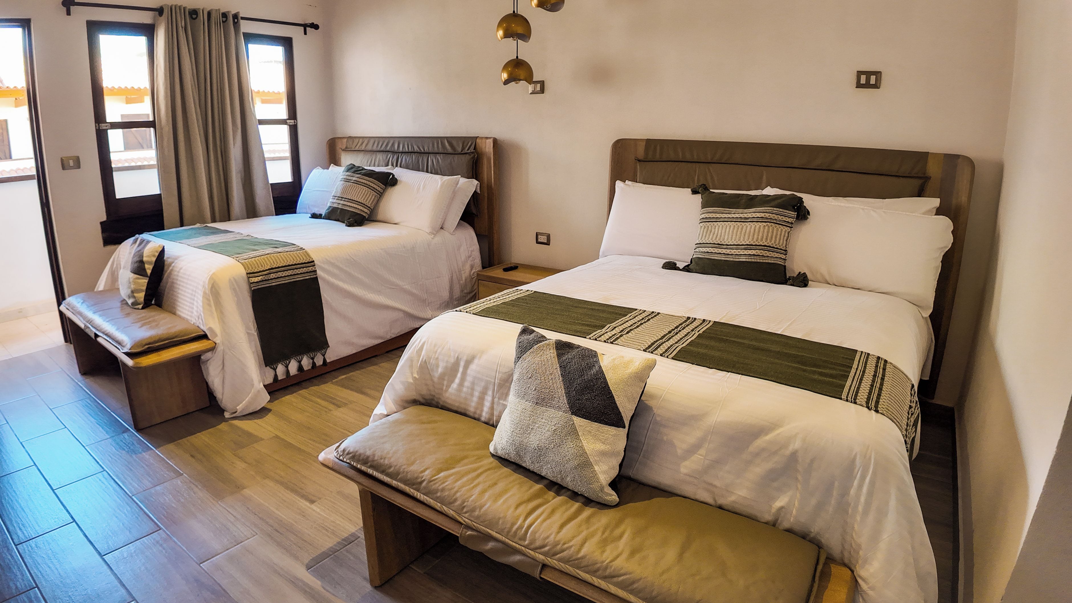 Habitación de hotel con dos camas, un banco y una ventana con cortinas.