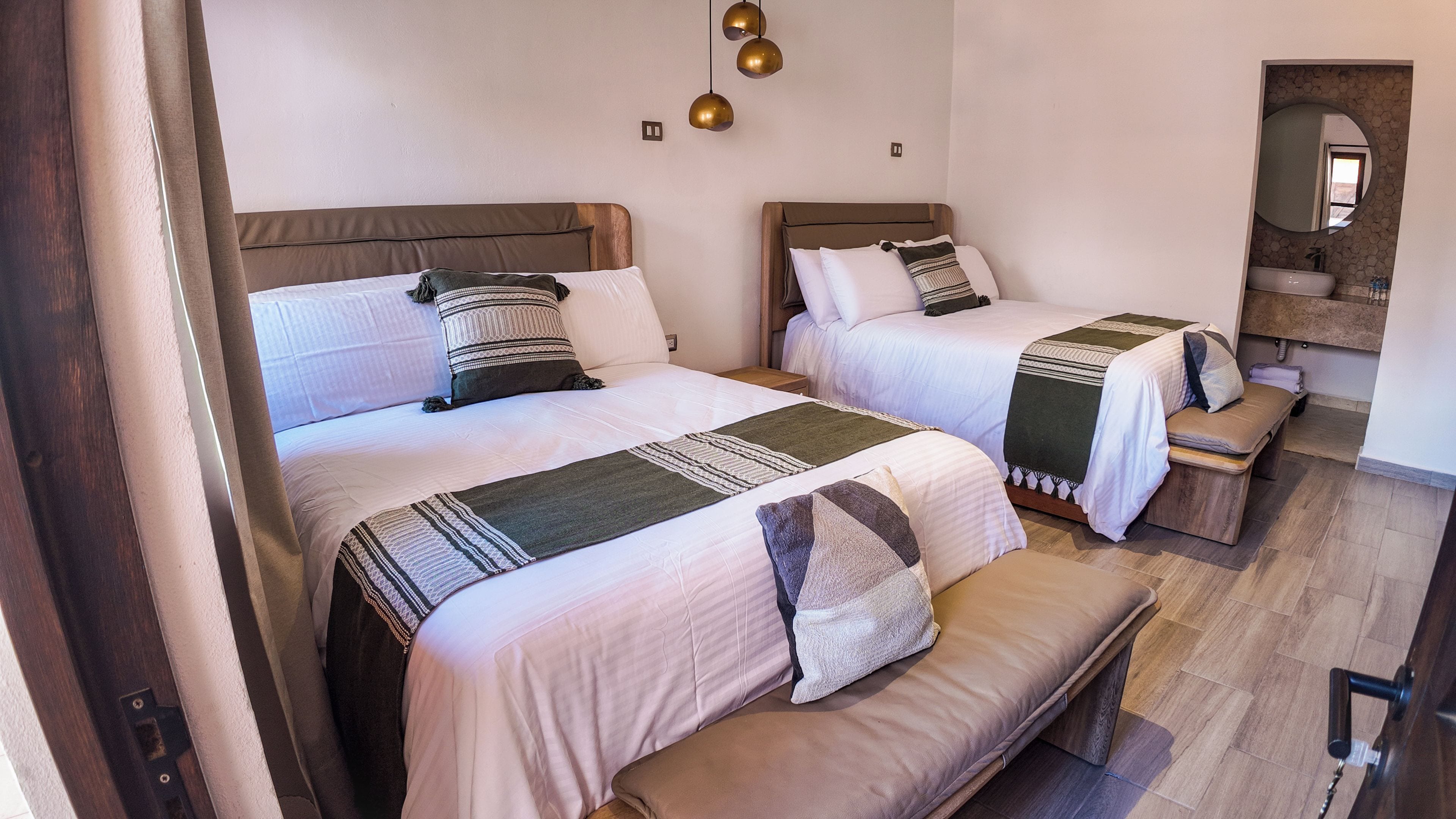 Una habitación de hotel con dos camas, un banco, una mesita y un espejo.