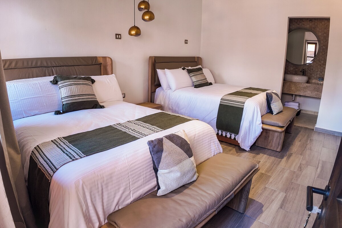 Ein Hotelzimmer mit zwei Betten, einer Bank, einem kleinen Tisch und einem Spiegel.