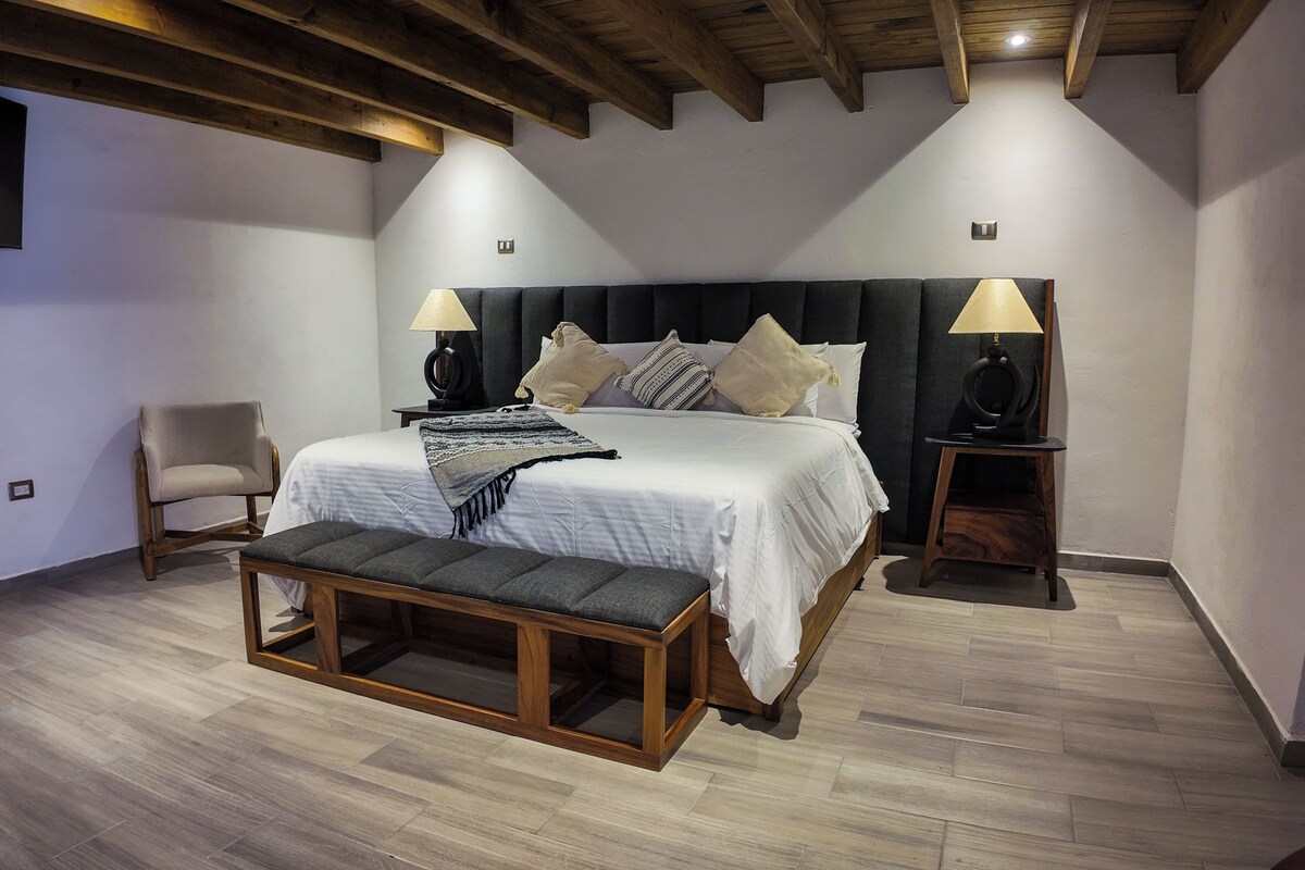 Ein Schlafzimmer mit Bett, Nachttischlampen, einem Sessel und einer Bank.