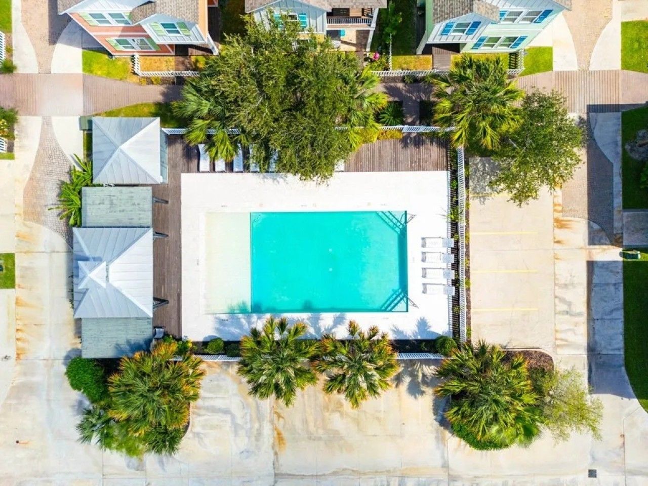 Vista aérea de uma piscina cercada por palmeiras e um estacionamento.
