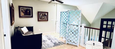 A room with a ceiling fan, a bed, a sofa, and a staircase leading to an upper level.