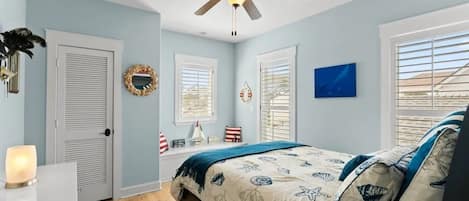 A bedroom with a bed, a ceiling fan, a window with blinds, a wall clock, and a decorative wreath.
